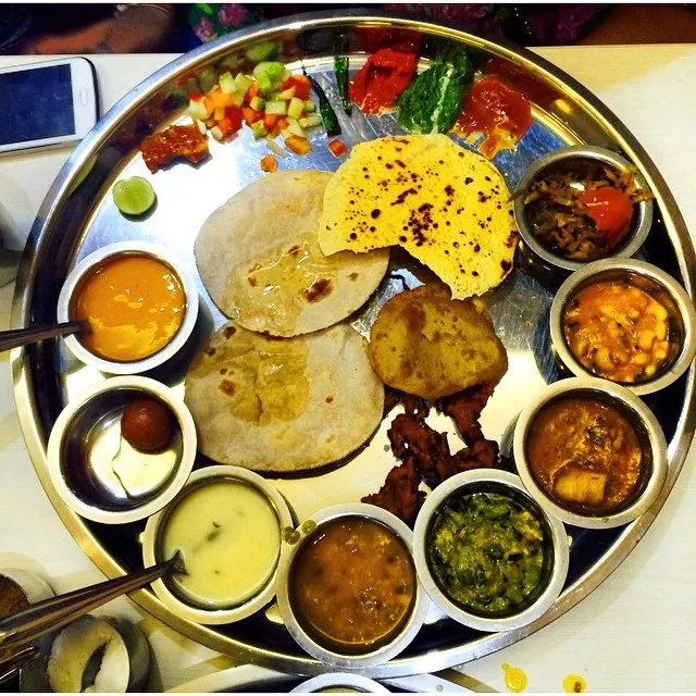 A Gujarati thali with small bowls of vegetables, dal, accompaniments, breads and sweets