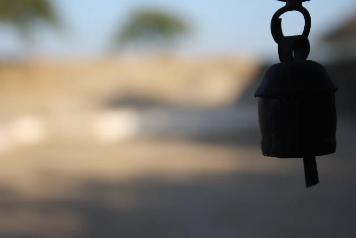 Handcrafted dark metal bell hanging against a blurred Kachchh landscape