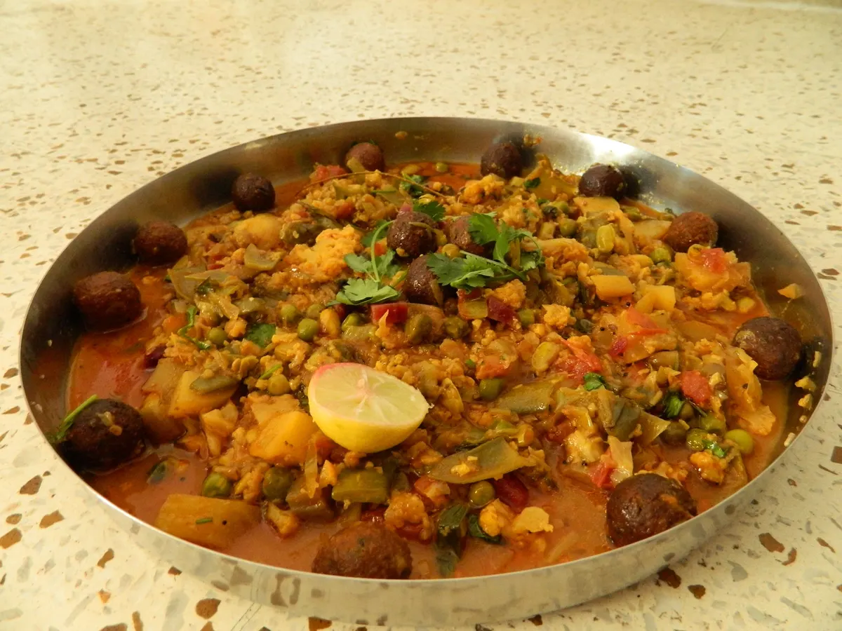 A metal serving dish filled with Gujarati undhiyu and vegetables